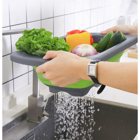 Person rinsing fresh vegetables in a green and gray foldable silicone basket over the sink, with water draining out